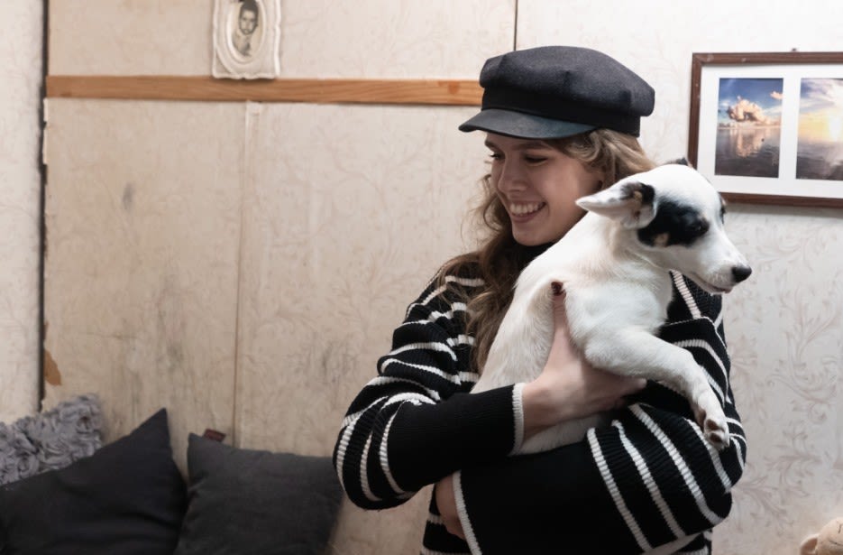 Kateryna smiles while holding a dog in the home of a family supported by Save the Children.